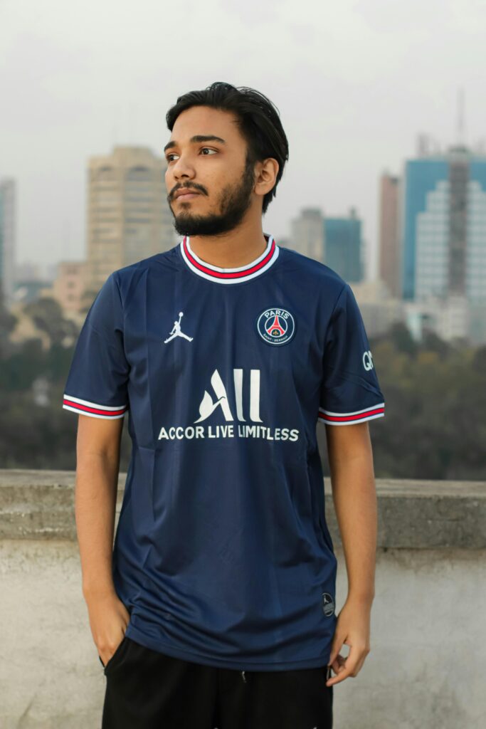 Young man wearing a sports jersey, standing outdoors with urban background.