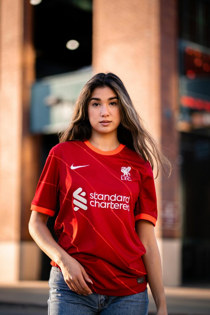 Portrait of a young woman posing confidently in a Liverpool FC shirt outdoors.